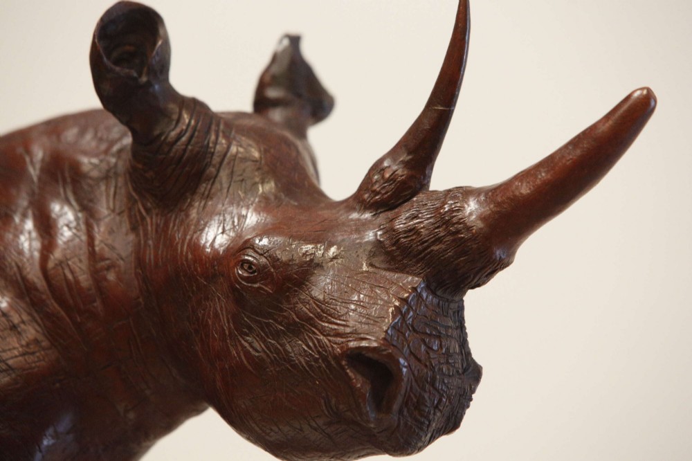 A carved reddish-brown ironwood sculpture of a rhinoceros mounted on a black metal display stand. View V