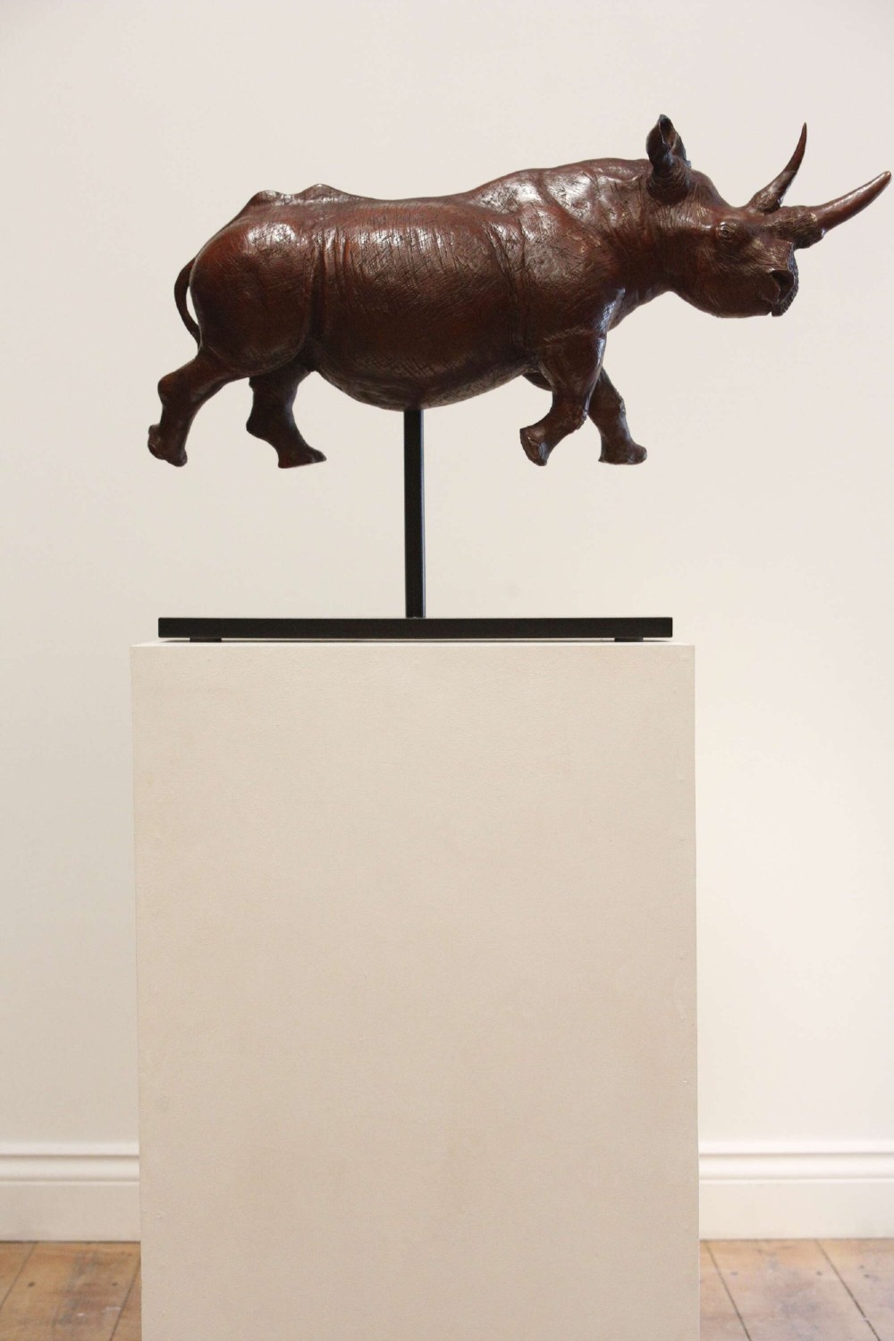 A carved reddish-brown ironwood sculpture of a rhinoceros mounted on a black metal display stand. View VI