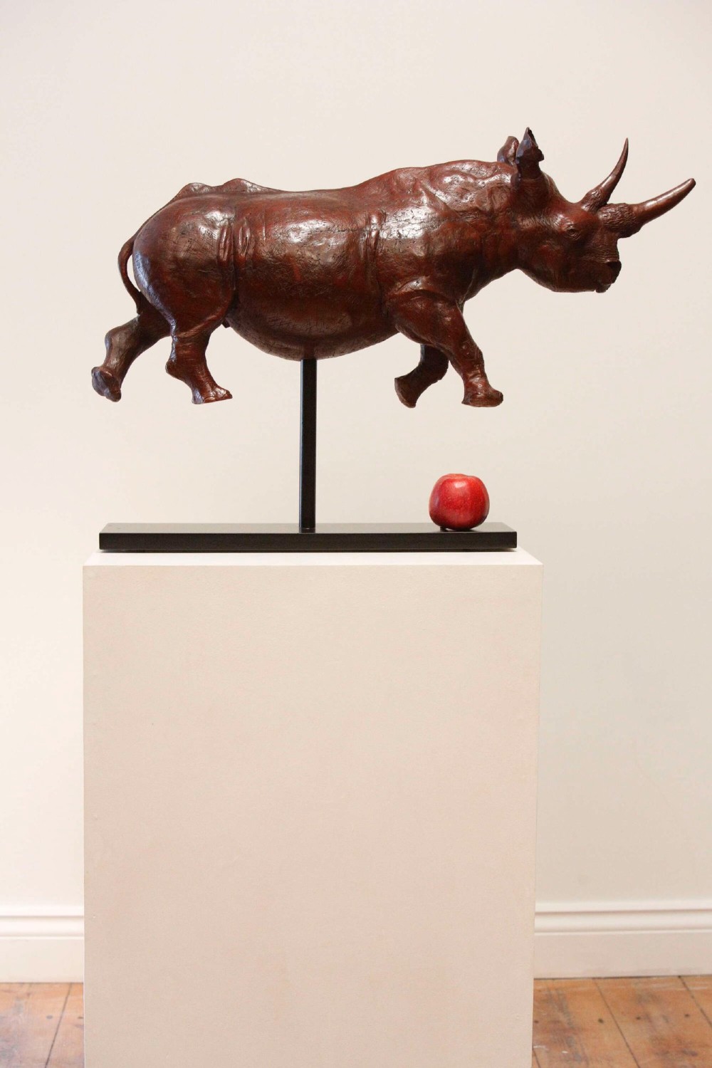 A carved reddish-brown ironwood sculpture of a rhinoceros mounted on a black metal display stand. View VII
