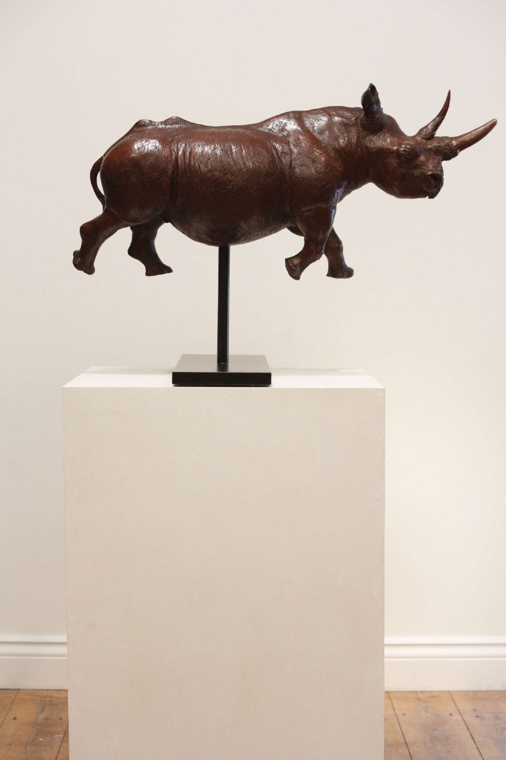 A carved reddish-brown ironwood sculpture of a rhinoceros mounted on a black metal display stand. View VIII