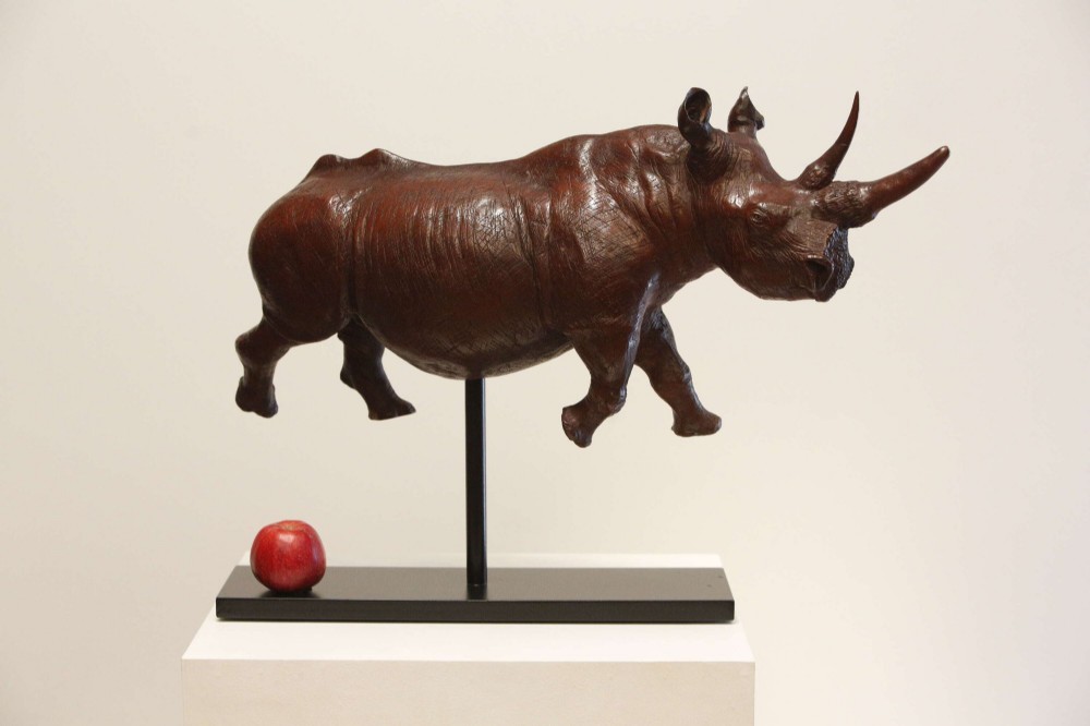 A carved reddish-brown ironwood sculpture of a rhinoceros mounted on a black metal display stand. View IX
