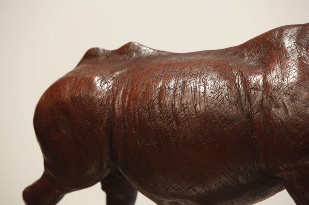 A carved reddish-brown ironwood sculpture of a rhinoceros mounted on a black metal display stand. View X