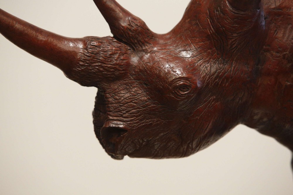 A carved reddish-brown ironwood sculpture of a rhinoceros mounted on a black metal display stand. View XII