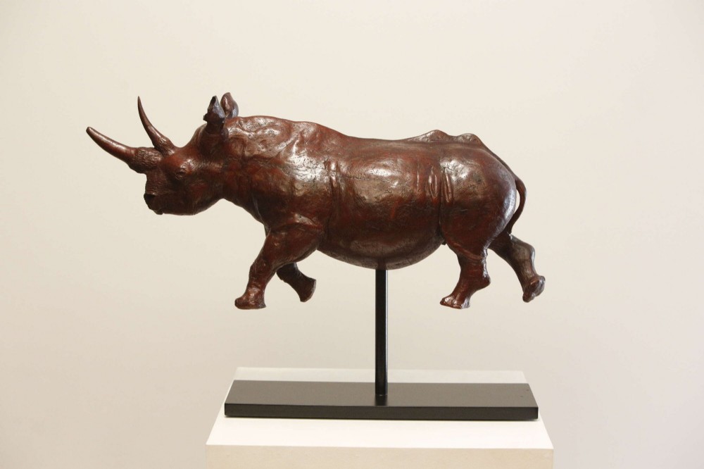 A carved reddish-brown ironwood sculpture of a rhinoceros mounted on a black metal display stand. View XIII