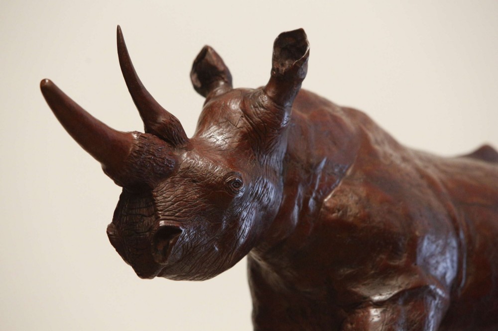 A carved reddish-brown ironwood sculpture of a rhinoceros mounted on a black metal display stand. View XV