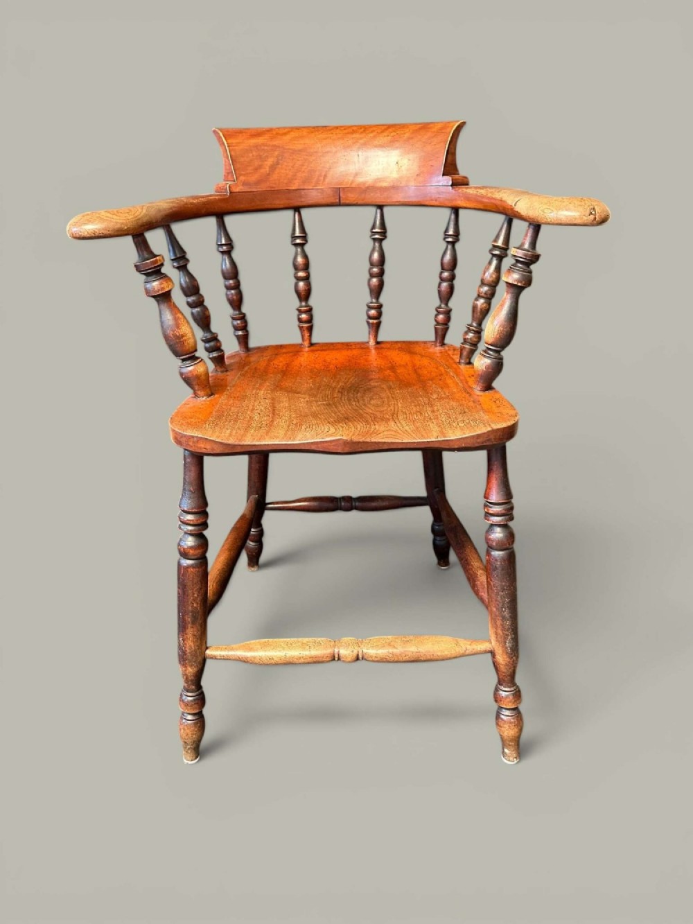 An antique alder wood Windsor captains chair featuring turned spindles, a contoured saddle seat, and high turned legs joined by stretchers.