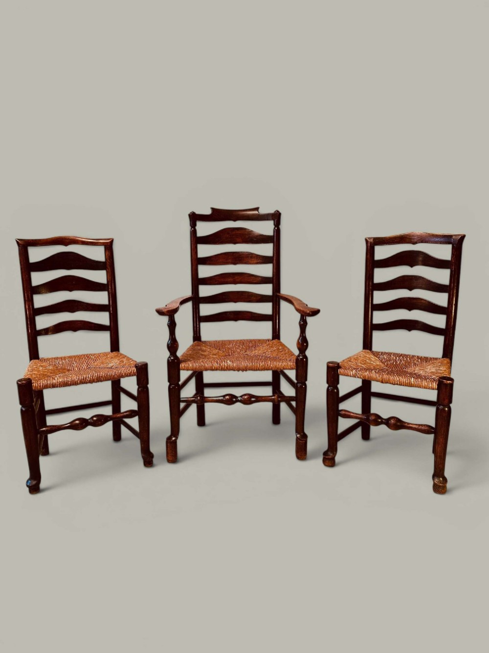 A set of dark brown ladder back dining chairs featuring woven rush seats, curved horizontal slats, and turned stretcher rails.