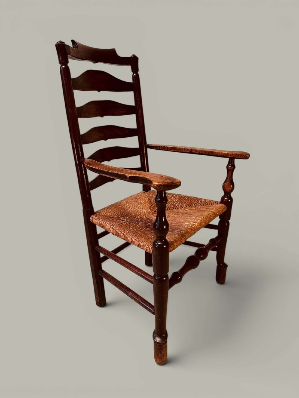 A set of dark brown ladder back dining chairs featuring woven rush seats, curved horizontal slats, and turned stretcher rails. View VI