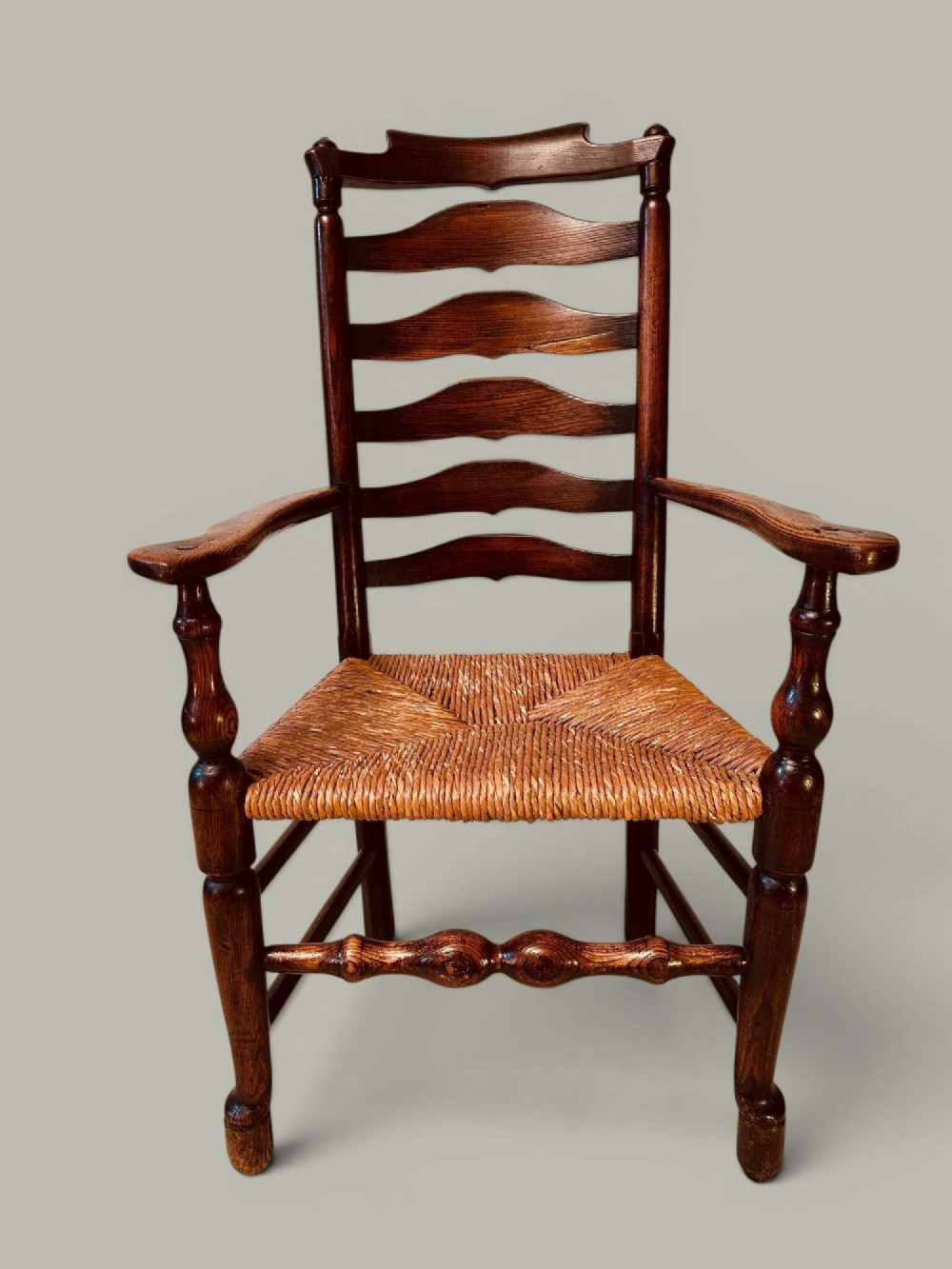 A set of dark brown ladder back dining chairs featuring woven rush seats, curved horizontal slats, and turned stretcher rails. View VII