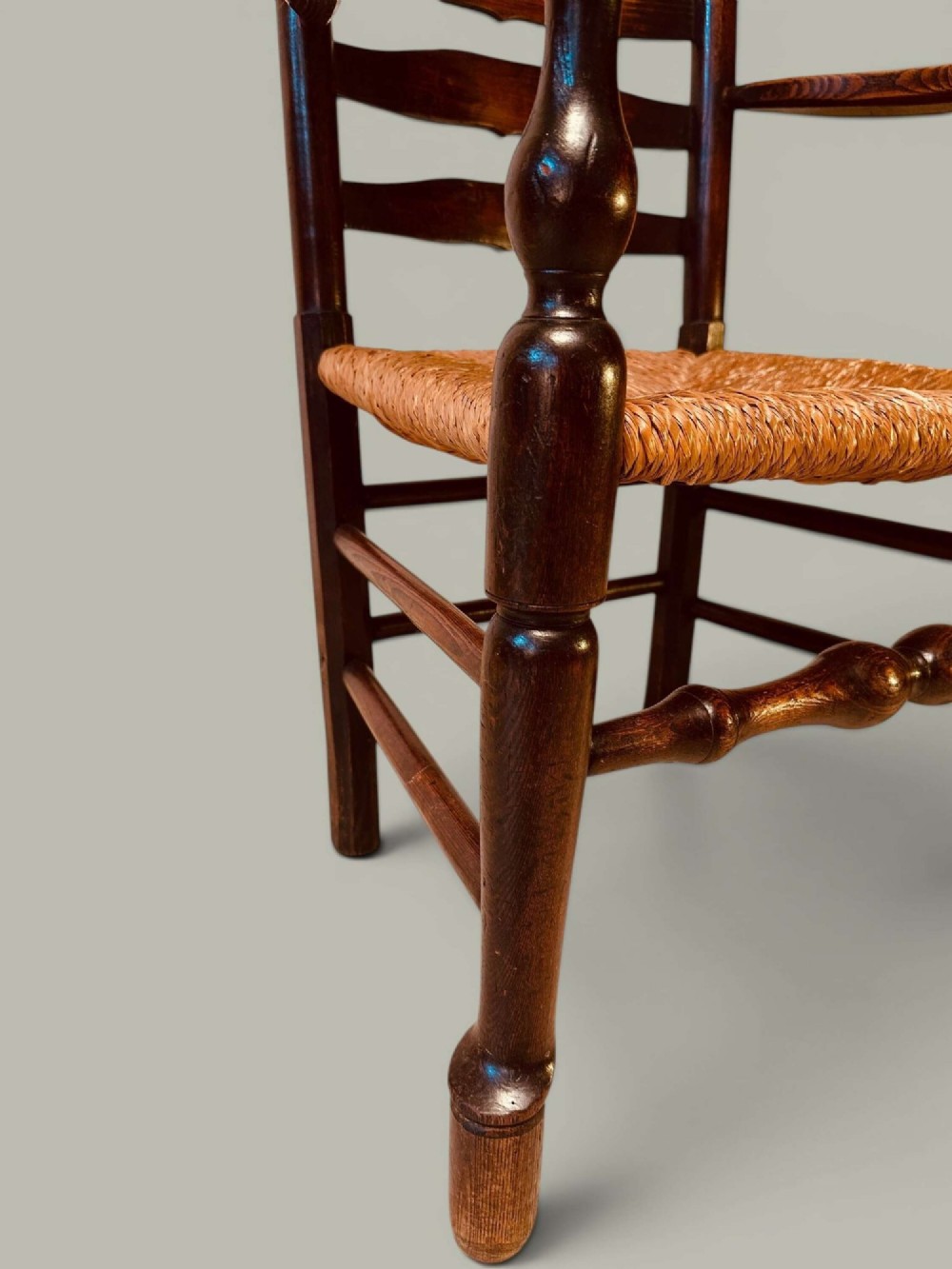 A set of dark brown ladder back dining chairs featuring woven rush seats, curved horizontal slats, and turned stretcher rails. View X