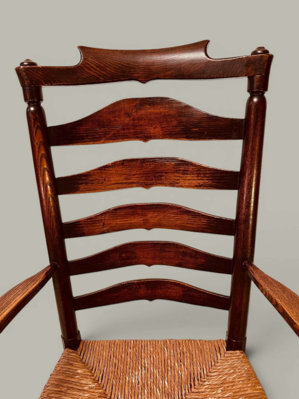 A set of dark brown ladder back dining chairs featuring woven rush seats, curved horizontal slats, and turned stretcher rails. View XII