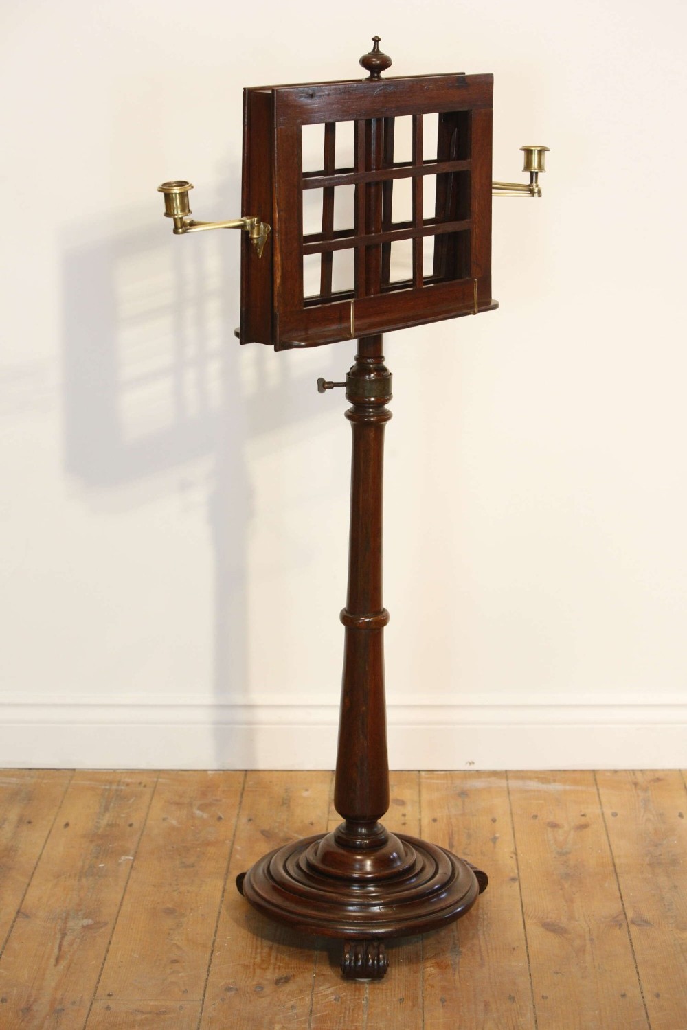 A 19th-century rosewood duet music stand with a double-sided lattice desk, brass candle sconces, an adjustable turned column, and a circular stepped base.