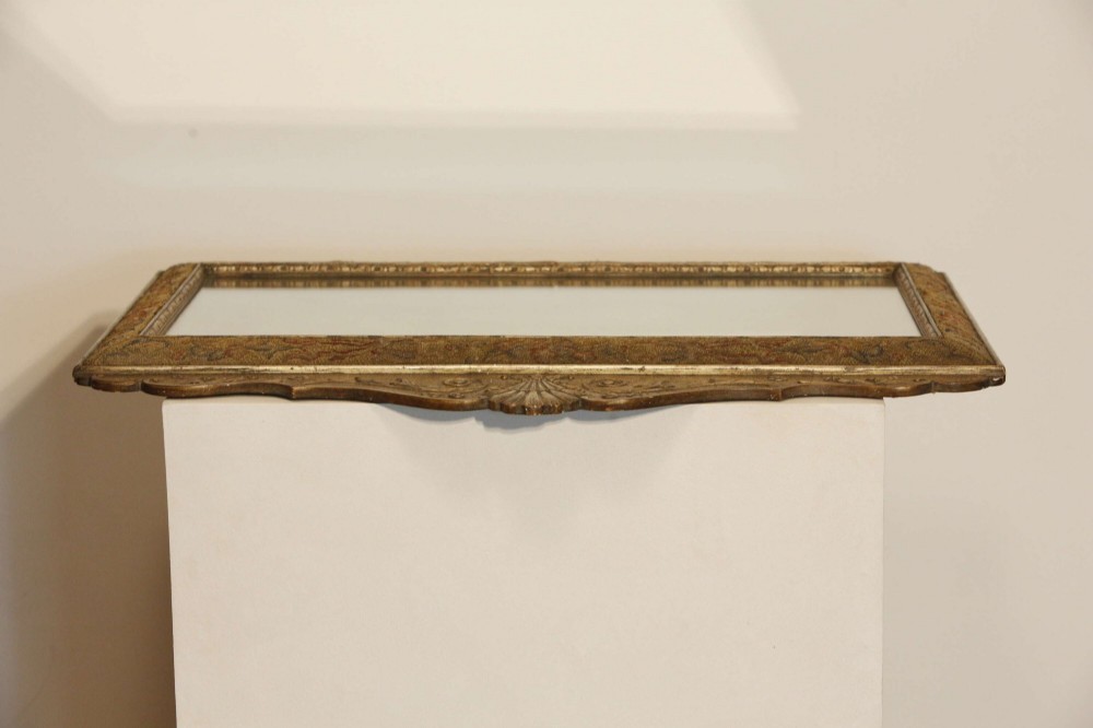 A 19th-century rectangular cushion wall mirror featuring an embroidered tapestry border, an ornamental gilt crest with a shell motif, and a glass plate. View XV