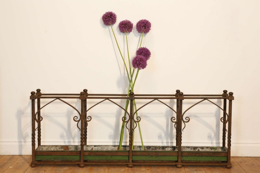 A rectangular Victorian Gothic Revival wrought iron umbrella stand featuring pointed tracery arches, twisted corner posts with ball finials, and a removable green metal drip tray. View VII