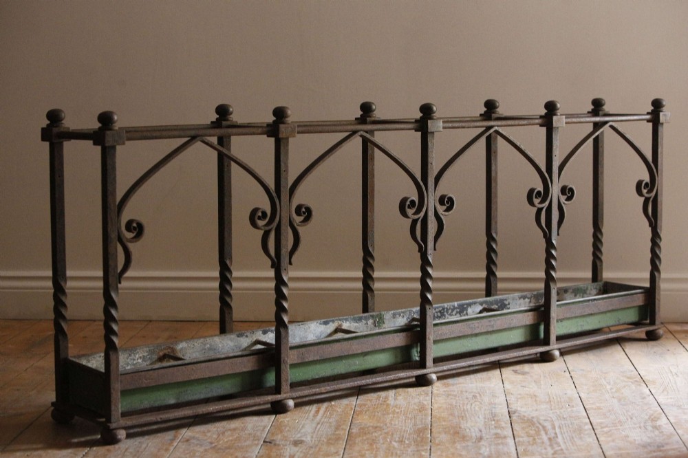 A rectangular Victorian Gothic Revival wrought iron umbrella stand featuring pointed tracery arches, twisted corner posts with ball finials, and a removable green metal drip tray. View VIII
