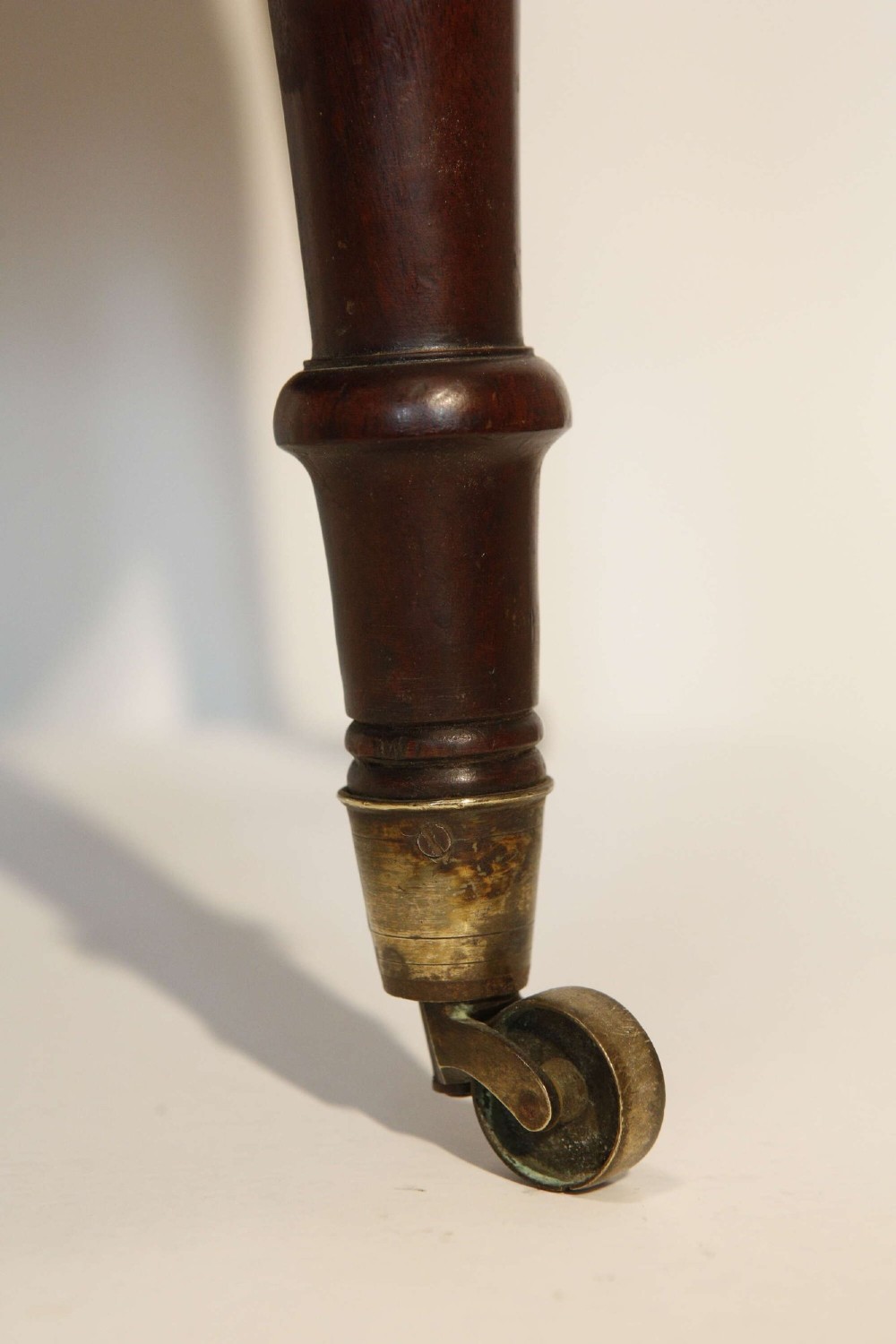 An oval mahogany wine cooler featuring twin brass binding, lion mask ring handles, tapered turned legs with brass castors, and a zinc liner. View IX