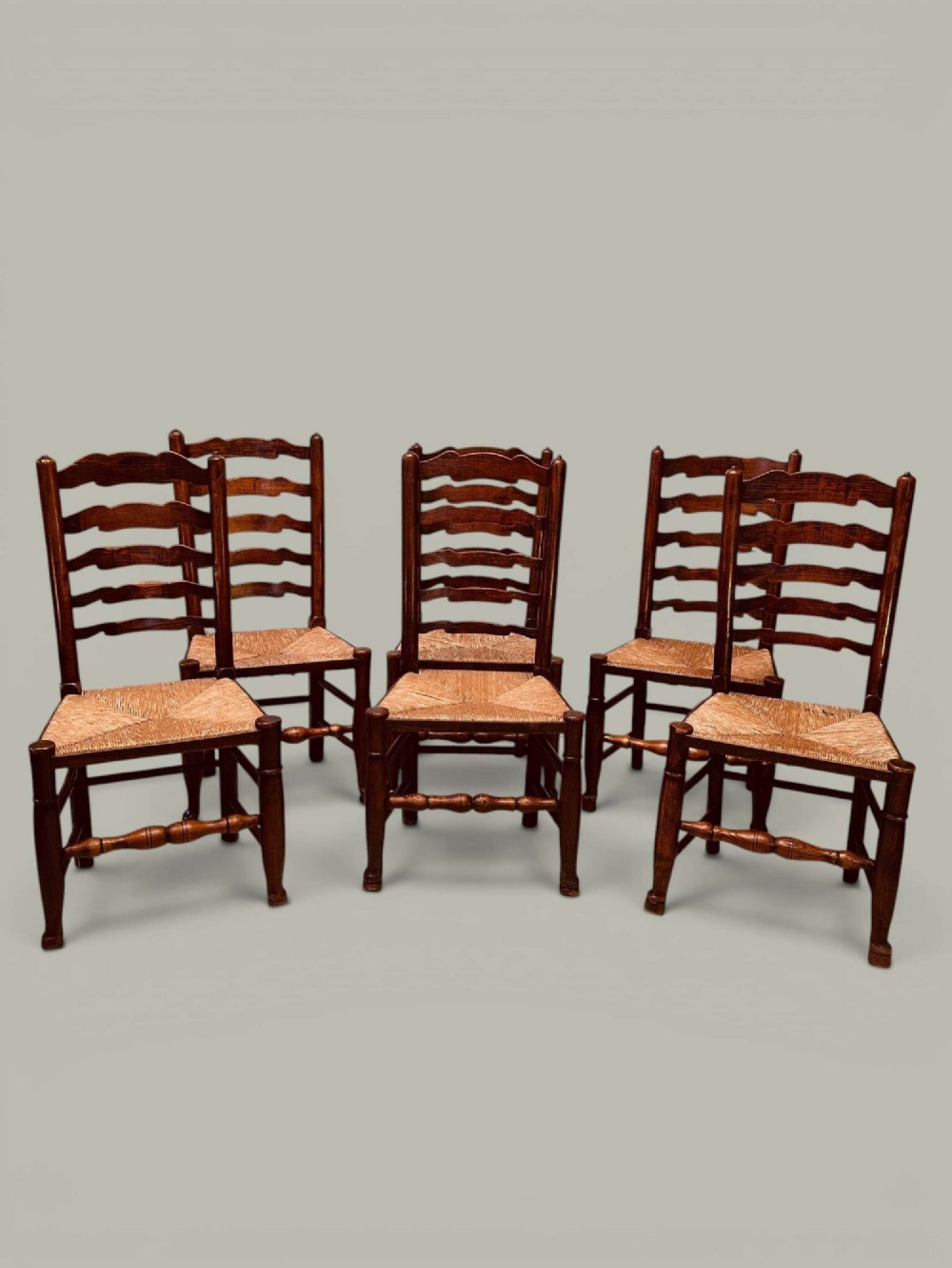 A set of eight antique ash dining chairs featuring wavy ladder backs, turned stretchers, and woven rush seats, comprising six side chairs and two carver armchairs. View V