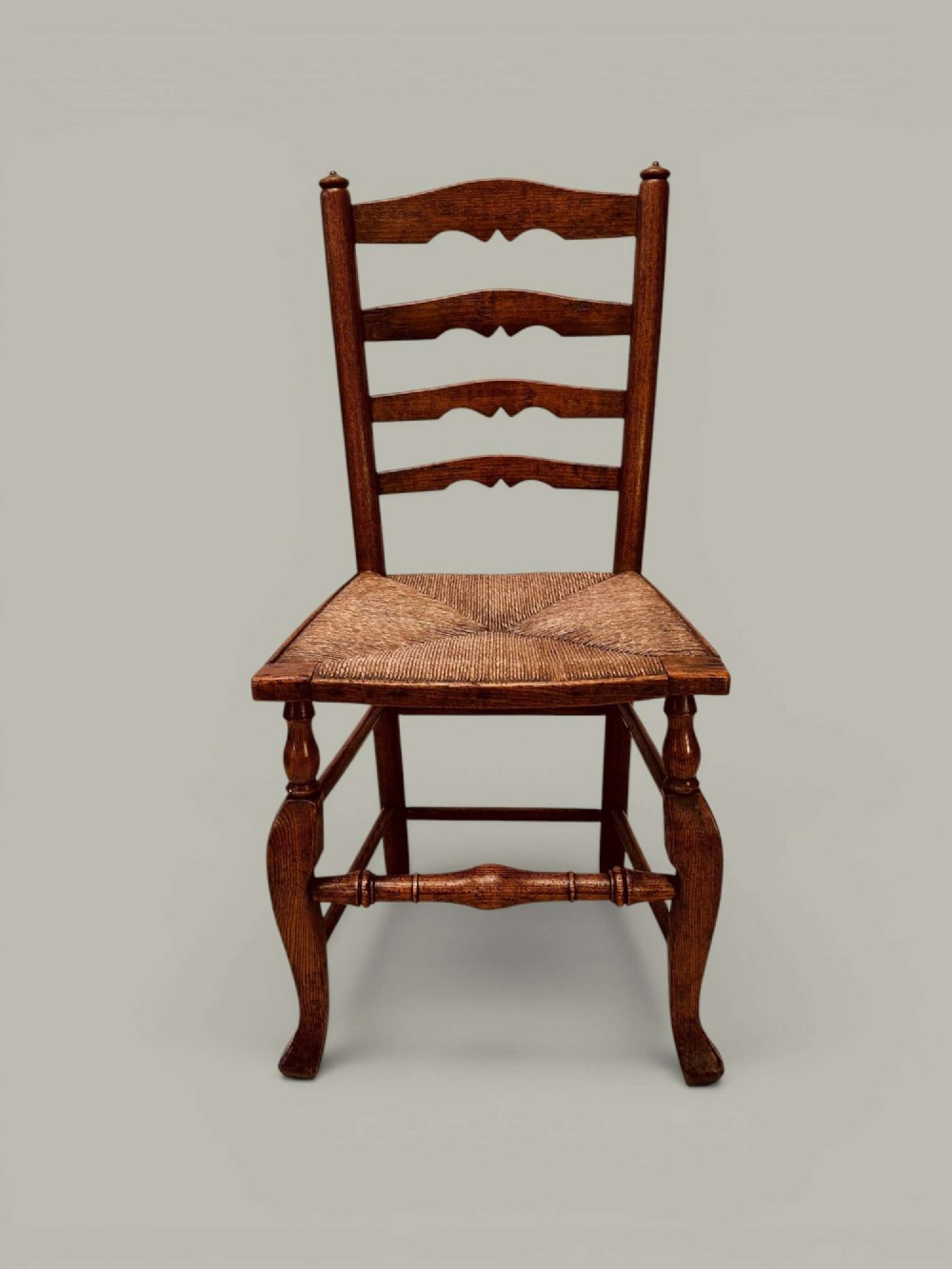 A pair of antique ash ladder back side chairs featuring shaped back rungs, woven rush seats, cabriole front legs, and turned stretchers. View II