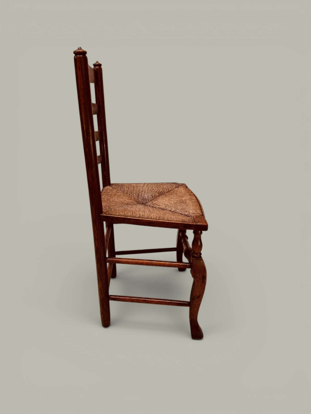 A pair of antique ash ladder back side chairs featuring shaped back rungs, woven rush seats, cabriole front legs, and turned stretchers. View V