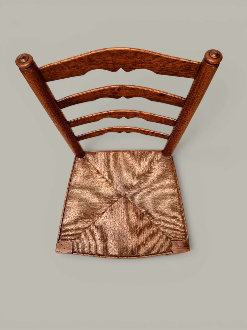 A pair of antique ash ladder back side chairs featuring shaped back rungs, woven rush seats, cabriole front legs, and turned stretchers. View VI