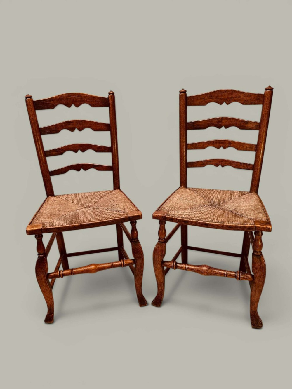A pair of antique ash ladder back side chairs featuring shaped back rungs, woven rush seats, cabriole front legs, and turned stretchers. View IX