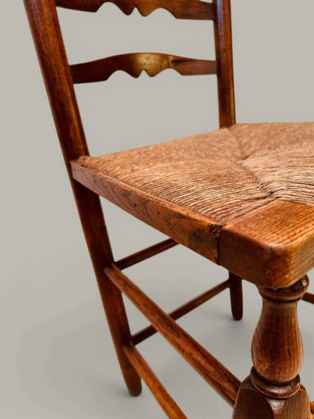 A pair of antique ash ladder back side chairs featuring shaped back rungs, woven rush seats, cabriole front legs, and turned stretchers. View XI