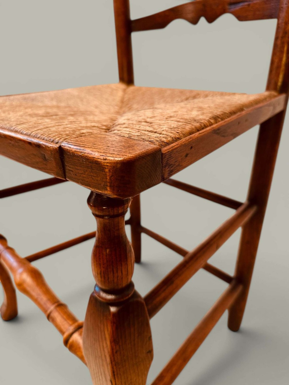 A pair of antique ash ladder back side chairs featuring shaped back rungs, woven rush seats, cabriole front legs, and turned stretchers. View XIII