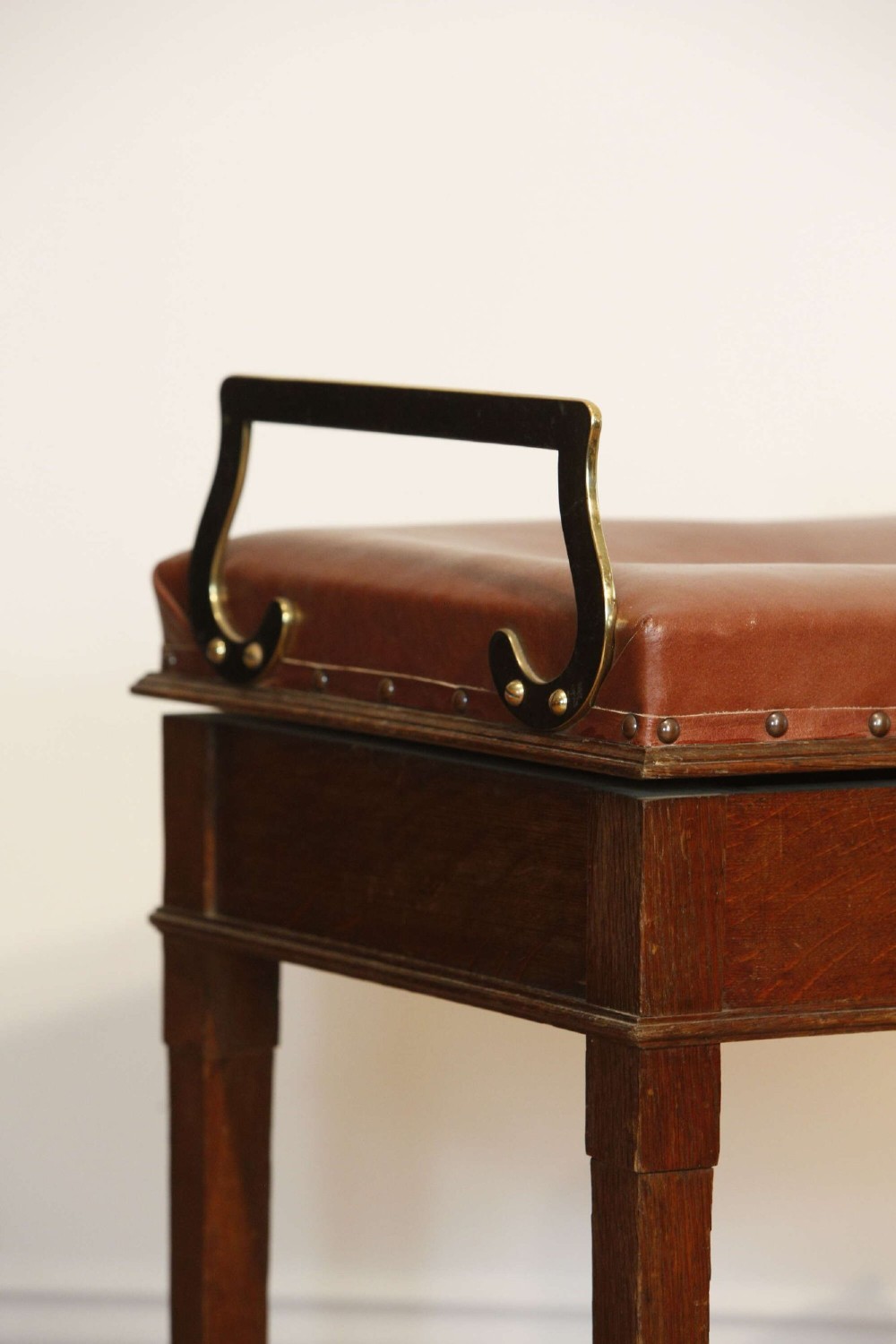 An Edwardian oak jockey scale featuring a padded brown leather seat with brass studs, brass side handles, and an integrated metal balance beam weighing mechanism. View V