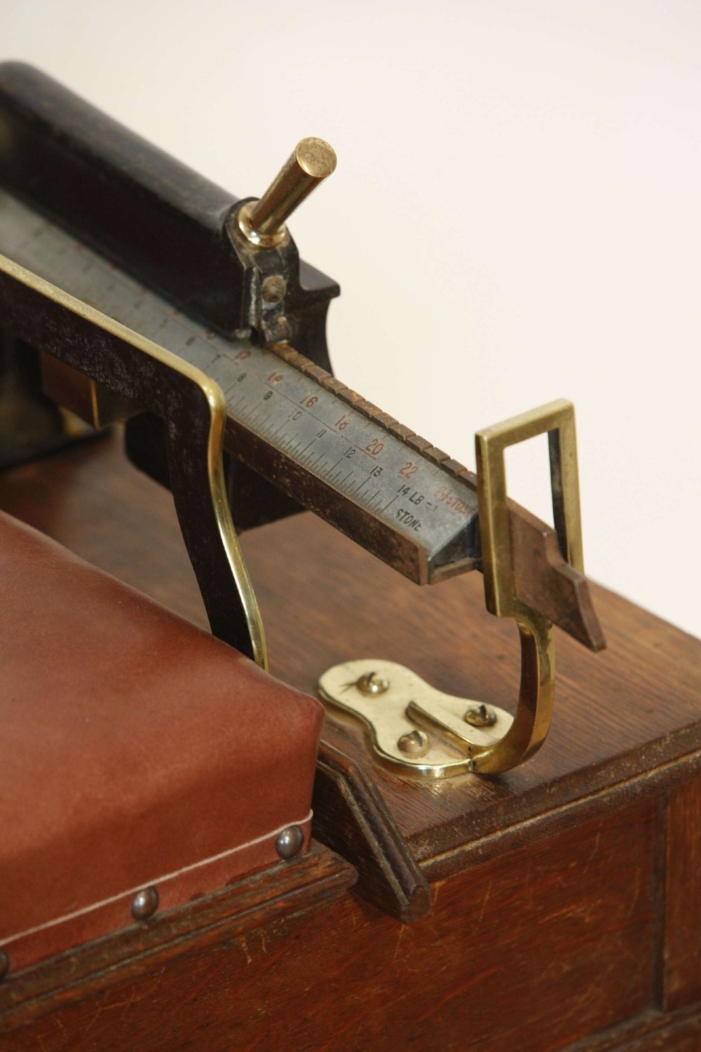 An Edwardian oak jockey scale featuring a padded brown leather seat with brass studs, brass side handles, and an integrated metal balance beam weighing mechanism. View VII