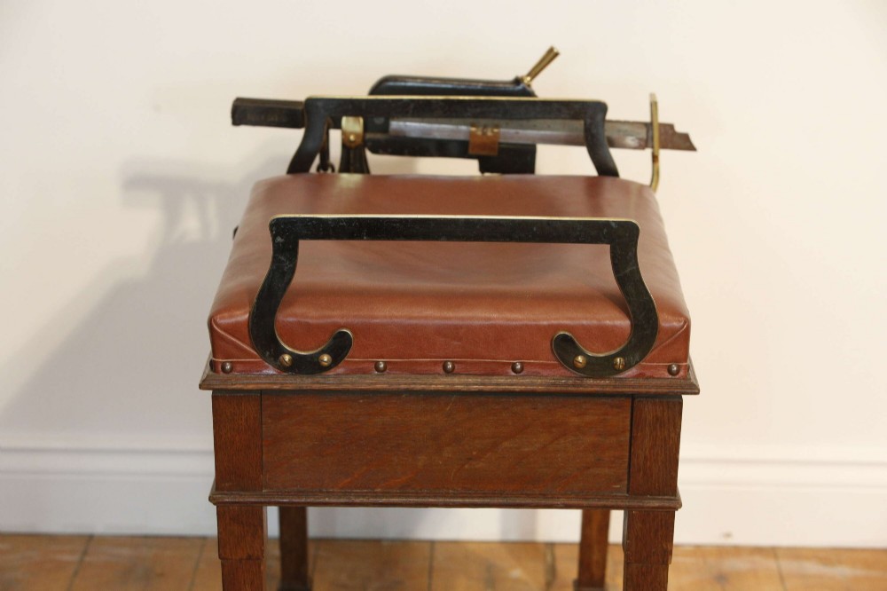 An Edwardian oak jockey scale featuring a padded brown leather seat with brass studs, brass side handles, and an integrated metal balance beam weighing mechanism. View VIII