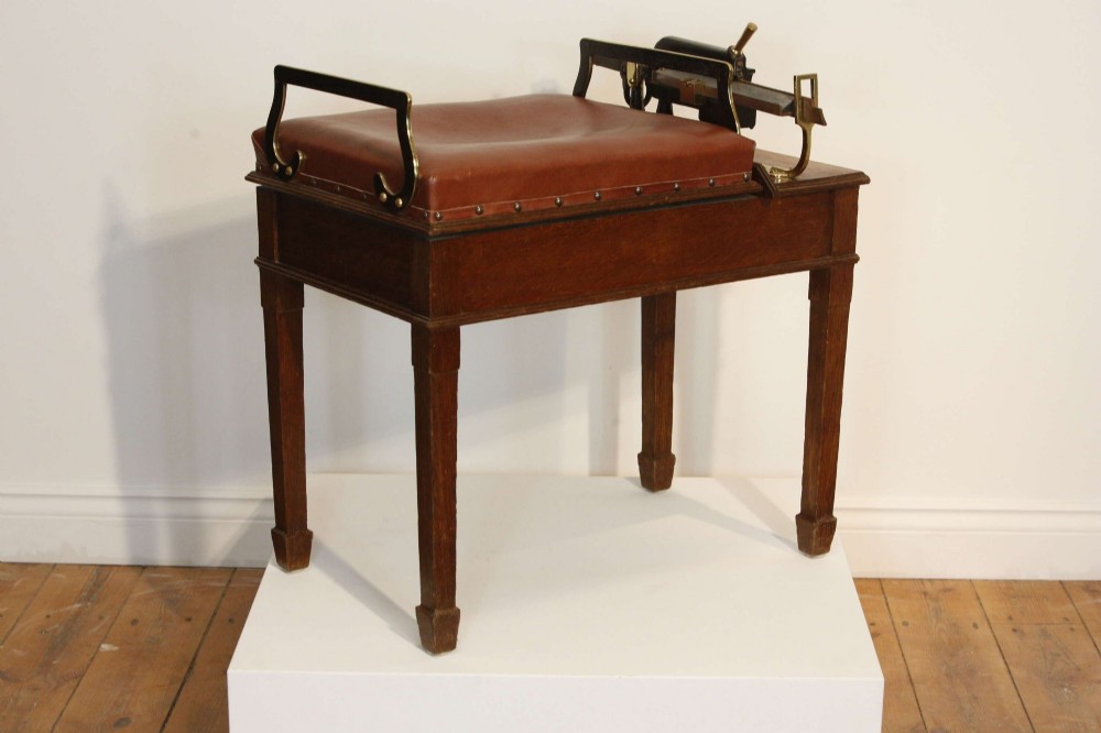 An Edwardian oak jockey scale featuring a padded brown leather seat with brass studs, brass side handles, and an integrated metal balance beam weighing mechanism. View IX