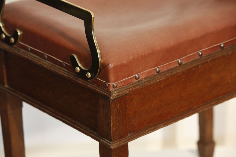 An Edwardian oak jockey scale featuring a padded brown leather seat with brass studs, brass side handles, and an integrated metal balance beam weighing mechanism. View X