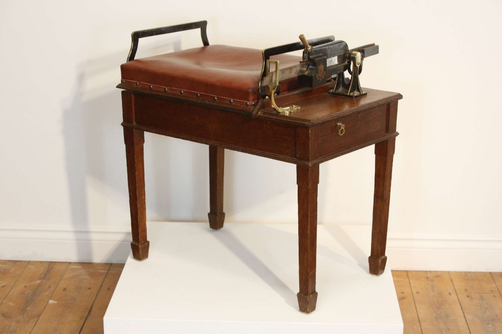 An Edwardian oak jockey scale featuring a padded brown leather seat with brass studs, brass side handles, and an integrated metal balance beam weighing mechanism. View XI