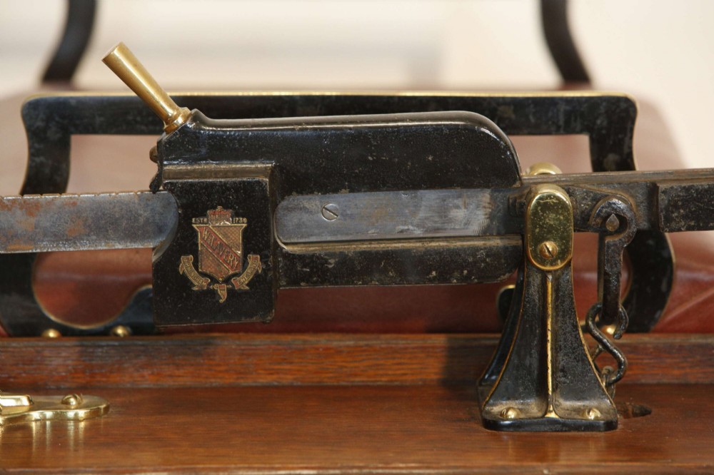 An Edwardian oak jockey scale featuring a padded brown leather seat with brass studs, brass side handles, and an integrated metal balance beam weighing mechanism. View XII