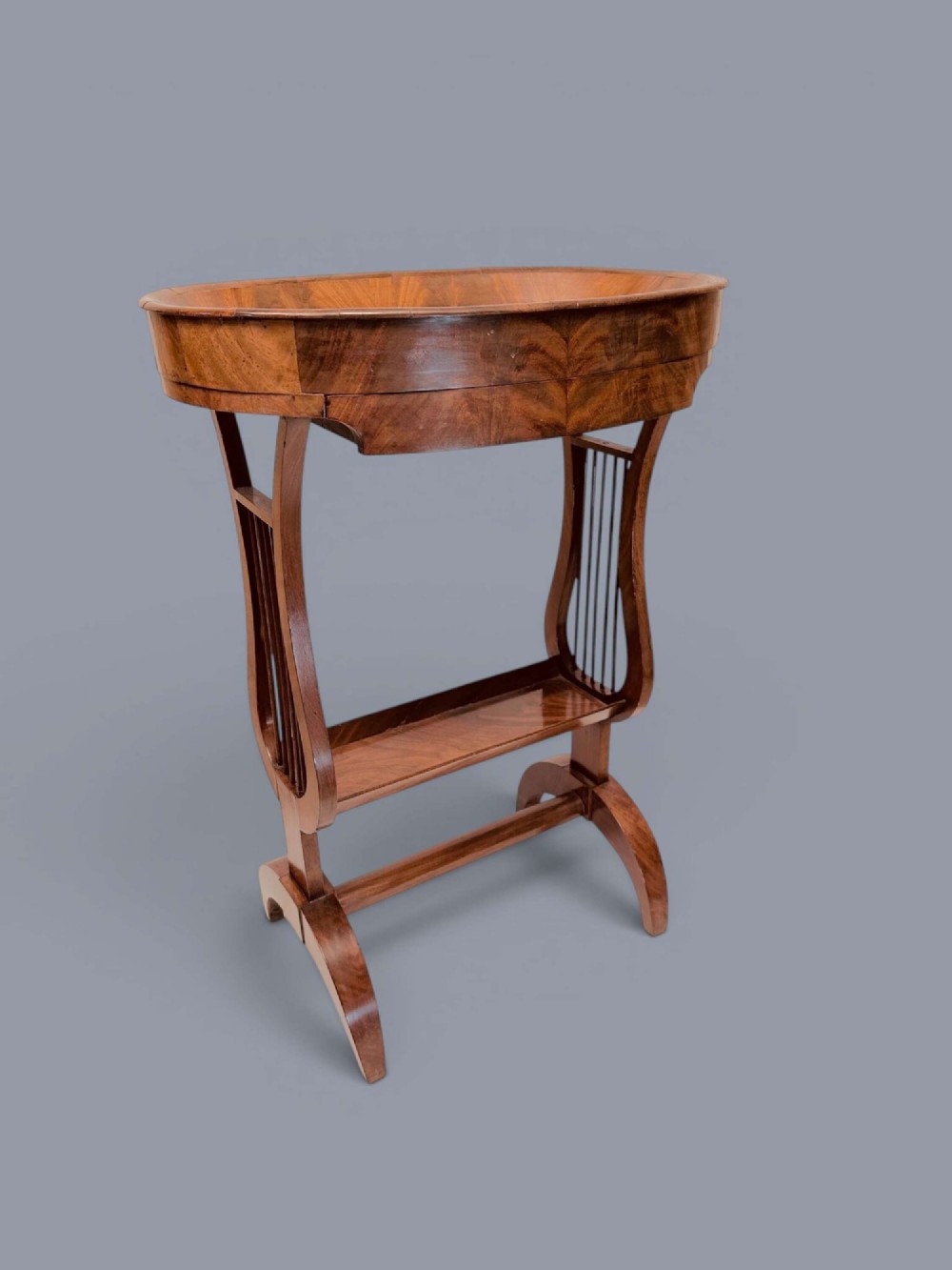A Regency period mahogany tricoteuse table featuring a gallery top rim, lyre-shaped leg supports with vertical rods, a lower shelf, and splayed feet.