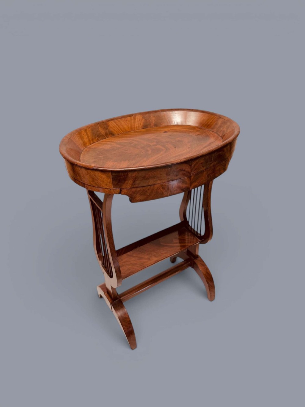 A Regency period mahogany tricoteuse table featuring a gallery top rim, lyre-shaped leg supports with vertical rods, a lower shelf, and splayed feet. View II