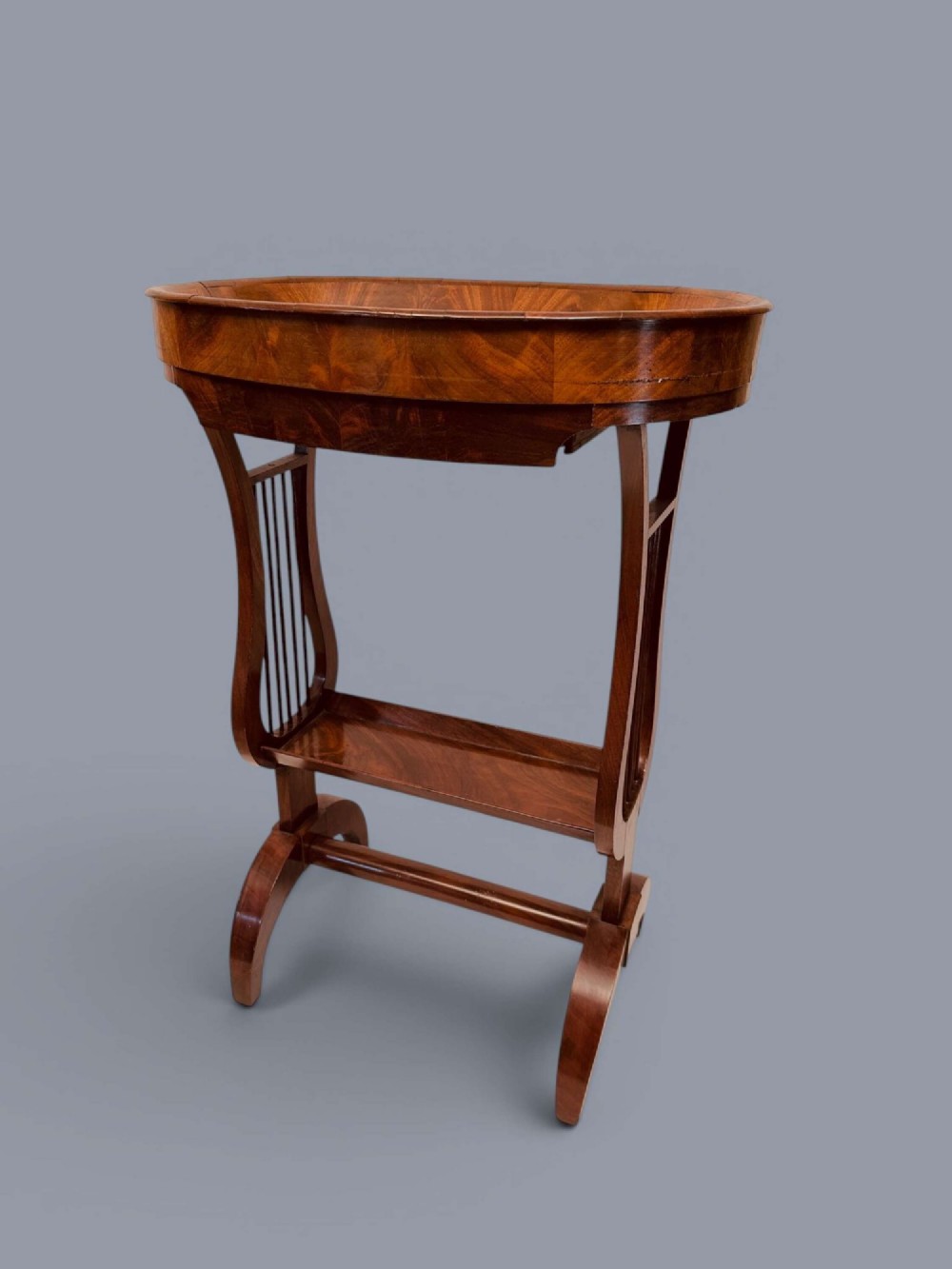 A Regency period mahogany tricoteuse table featuring a gallery top rim, lyre-shaped leg supports with vertical rods, a lower shelf, and splayed feet. View IV