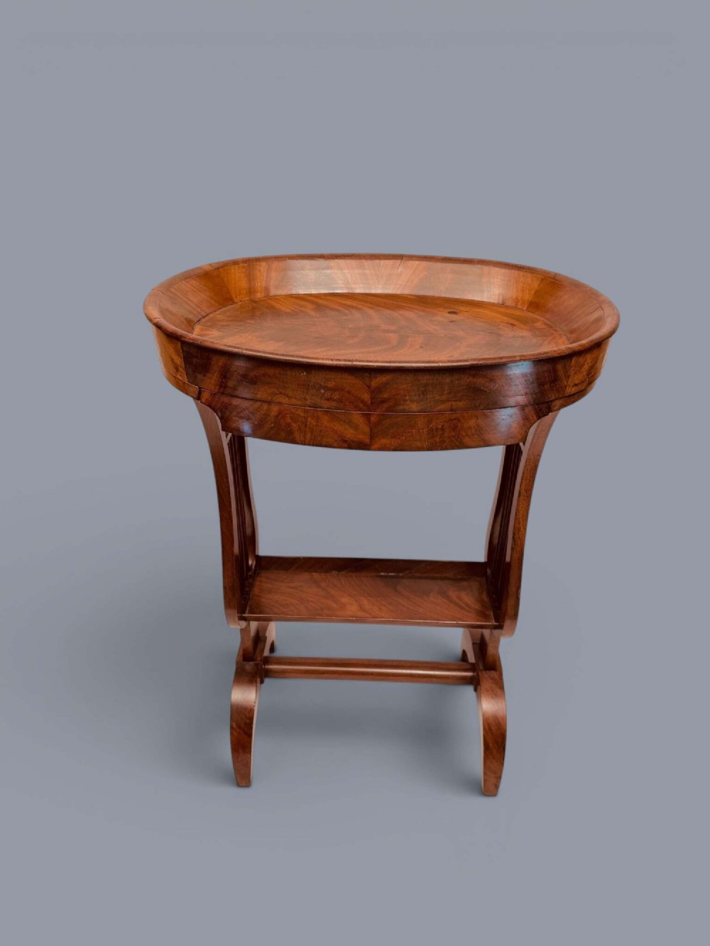 A Regency period mahogany tricoteuse table featuring a gallery top rim, lyre-shaped leg supports with vertical rods, a lower shelf, and splayed feet. View V