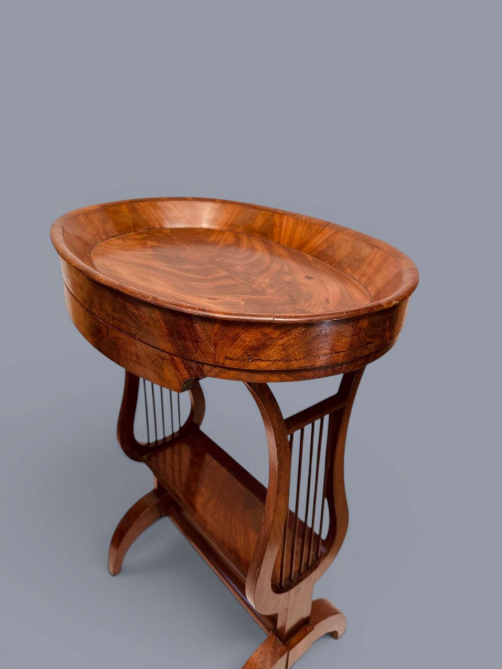 A Regency period mahogany tricoteuse table featuring a gallery top rim, lyre-shaped leg supports with vertical rods, a lower shelf, and splayed feet. View XI