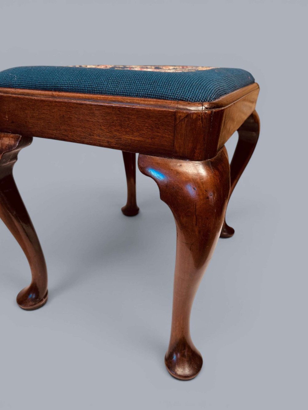 A rectangular red walnut stool with carved cabriole legs, pad feet, and a navy blue needlepoint upholstered seat featuring a central floral wreath motif. View XI