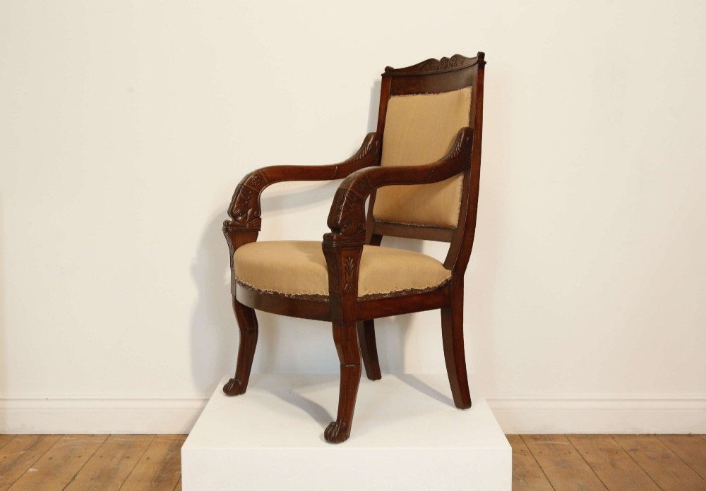 An early nineteenth-century French Empire carved mahogany armchair with padded seat and backrest, curved arms, and carved front legs.