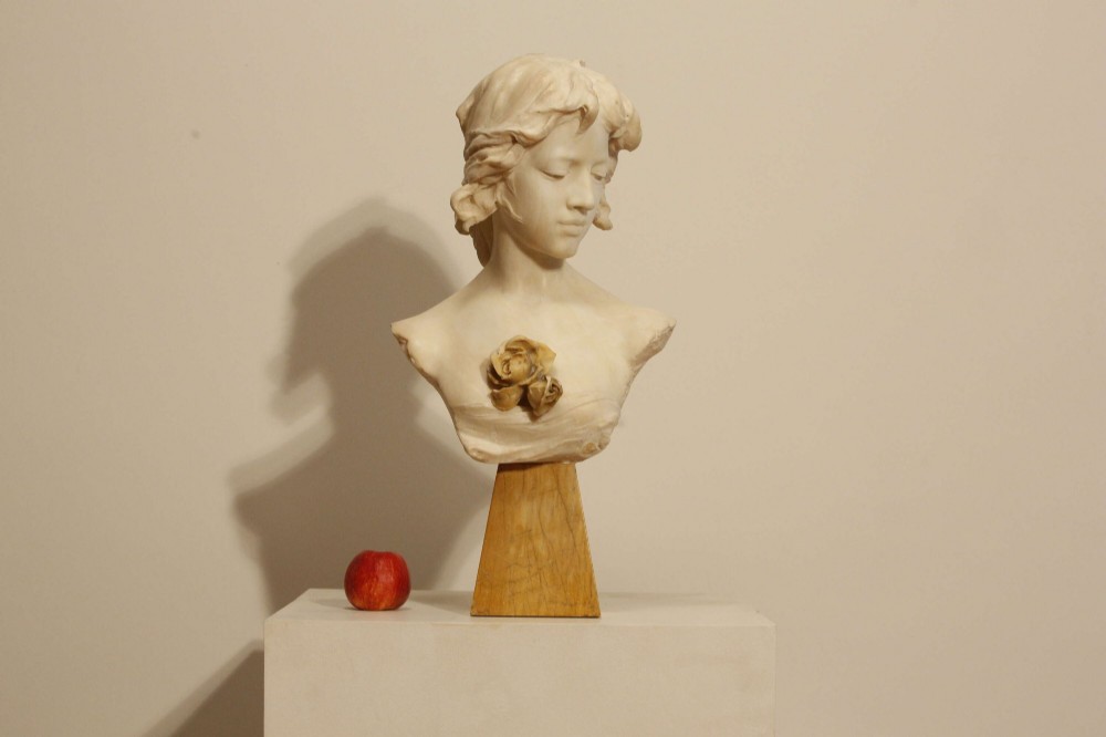 An early twentieth-century carved Carrara marble bust depicting a young female subject with a carved floral corsage, mounted on a wooden pedestal base.