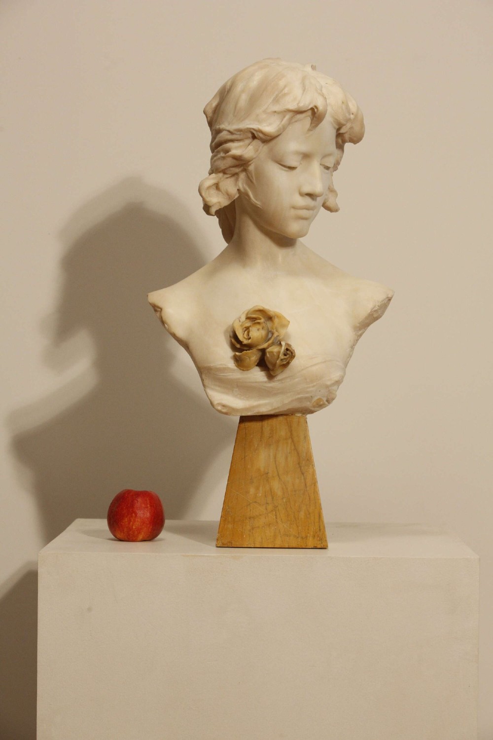 An early twentieth-century carved Carrara marble bust depicting a young female subject with a carved floral corsage, mounted on a wooden pedestal base. View II
