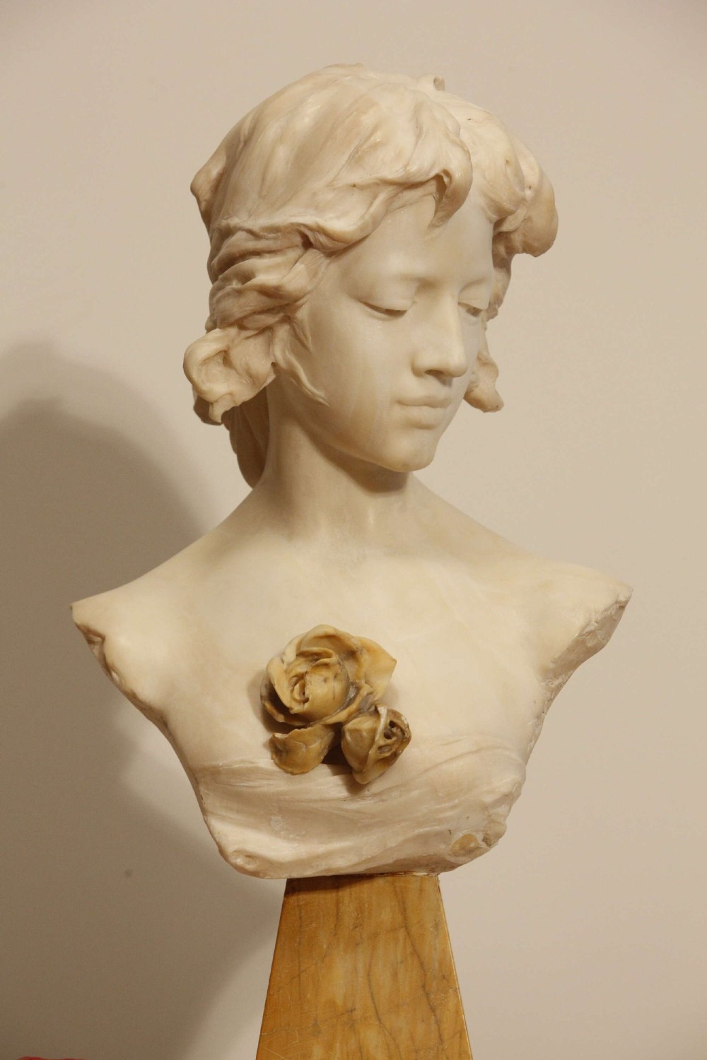 An early twentieth-century carved Carrara marble bust depicting a young female subject with a carved floral corsage, mounted on a wooden pedestal base. View III
