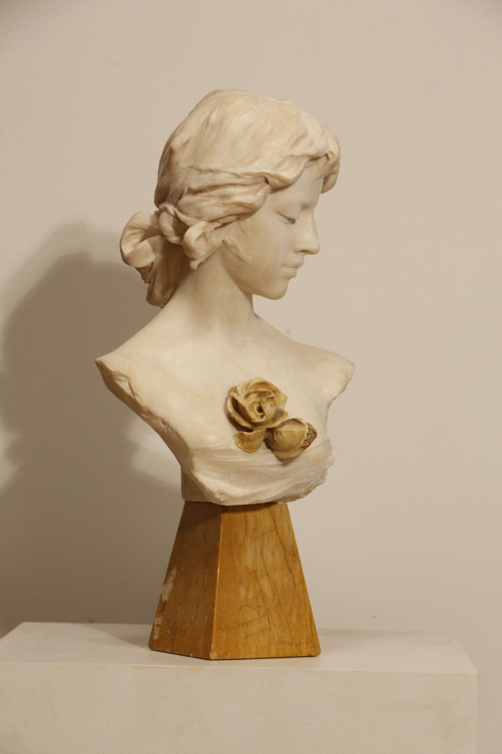 An early twentieth-century carved Carrara marble bust depicting a young female subject with a carved floral corsage, mounted on a wooden pedestal base. View V