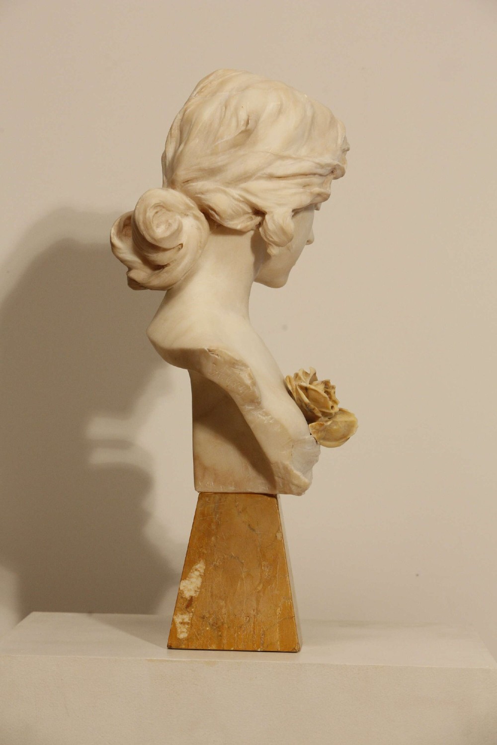 An early twentieth-century carved Carrara marble bust depicting a young female subject with a carved floral corsage, mounted on a wooden pedestal base. View VI