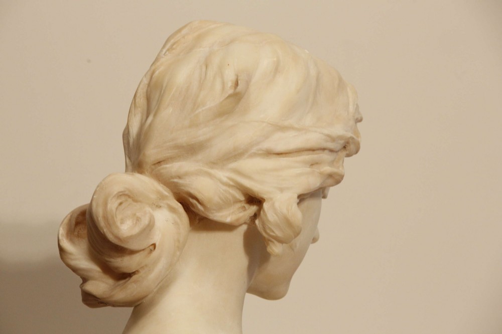 An early twentieth-century carved Carrara marble bust depicting a young female subject with a carved floral corsage, mounted on a wooden pedestal base. View VII