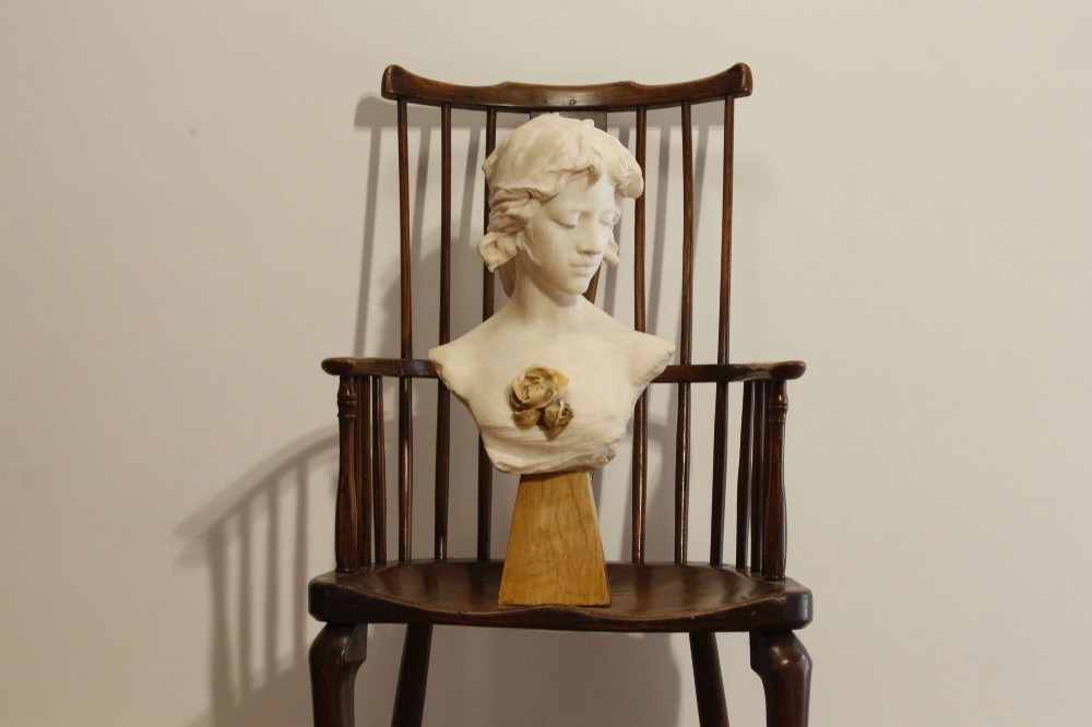 An early twentieth-century carved Carrara marble bust depicting a young female subject with a carved floral corsage, mounted on a wooden pedestal base. View XI