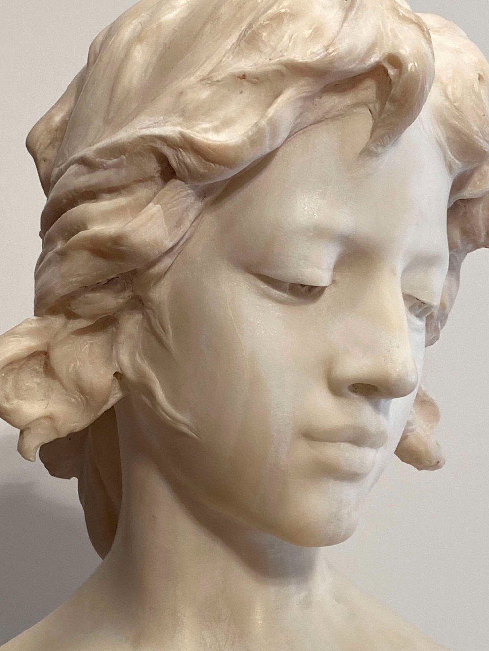 An early twentieth-century carved Carrara marble bust depicting a young female subject with a carved floral corsage, mounted on a wooden pedestal base. View XII
