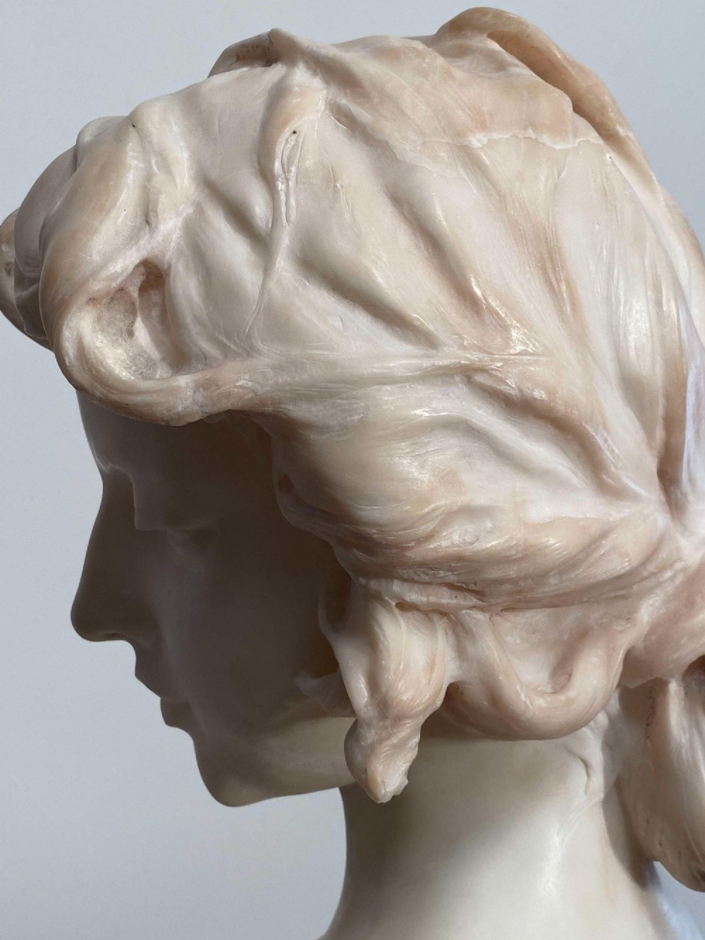 An early twentieth-century carved Carrara marble bust depicting a young female subject with a carved floral corsage, mounted on a wooden pedestal base. View XIII